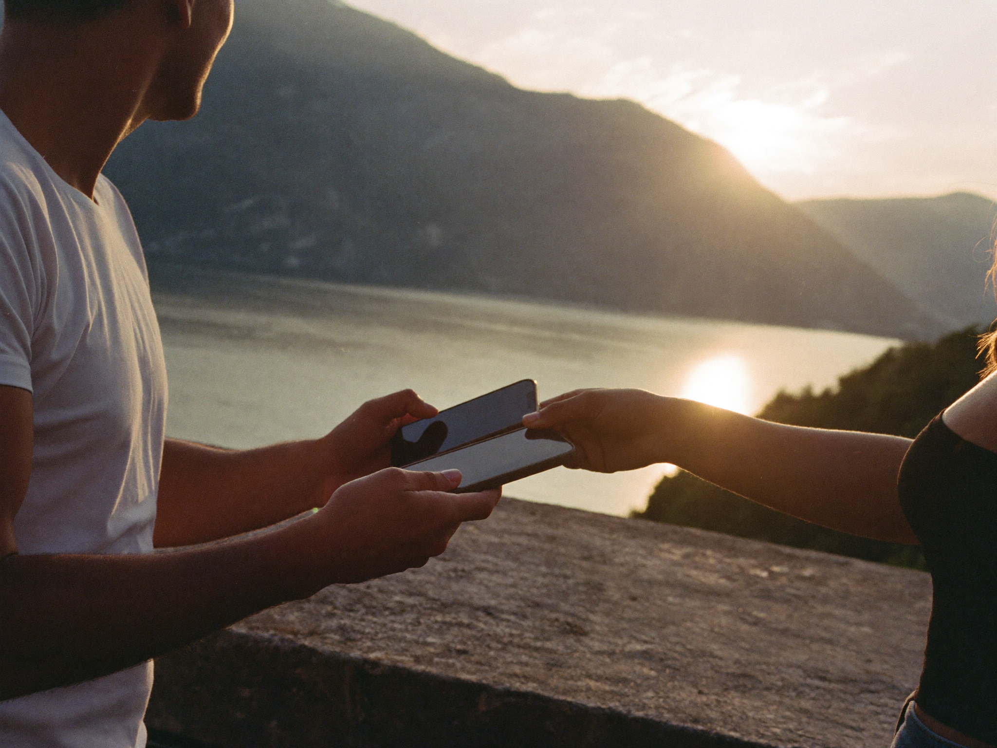 Zwei Menschen tauschen Kontakte mit ihren Smartphones am Gardasee bei Sonnenuntergang